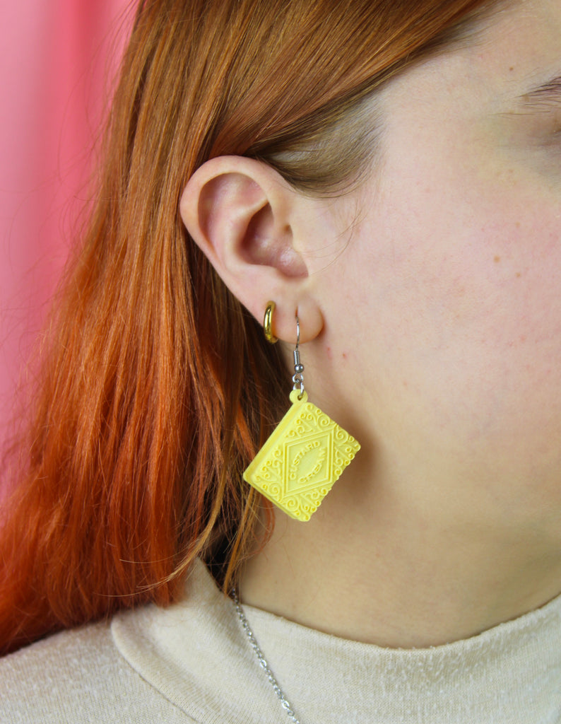Custard cream earrings worn by a person with red hair.