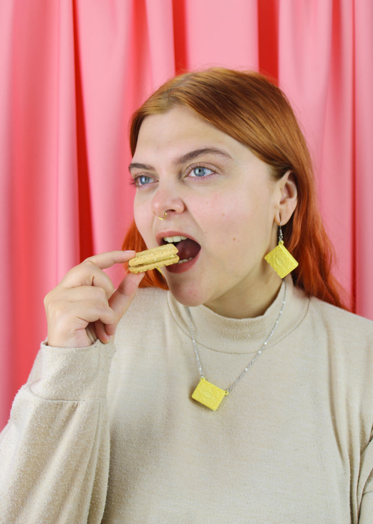 Woman with red hair eating a cookie against a pink curtain background
