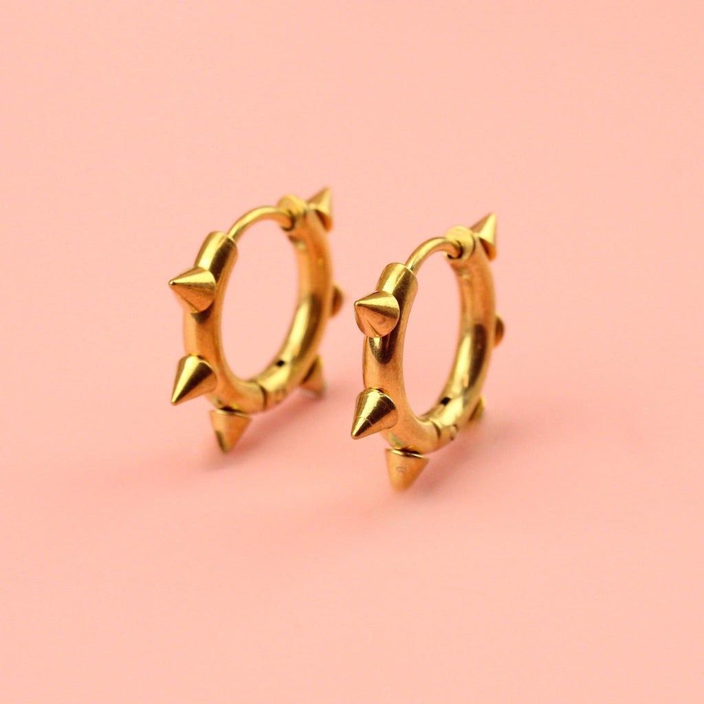 Gold plated stainless steel huggie hoops with punk-inspired spikes surrounding the edge 
