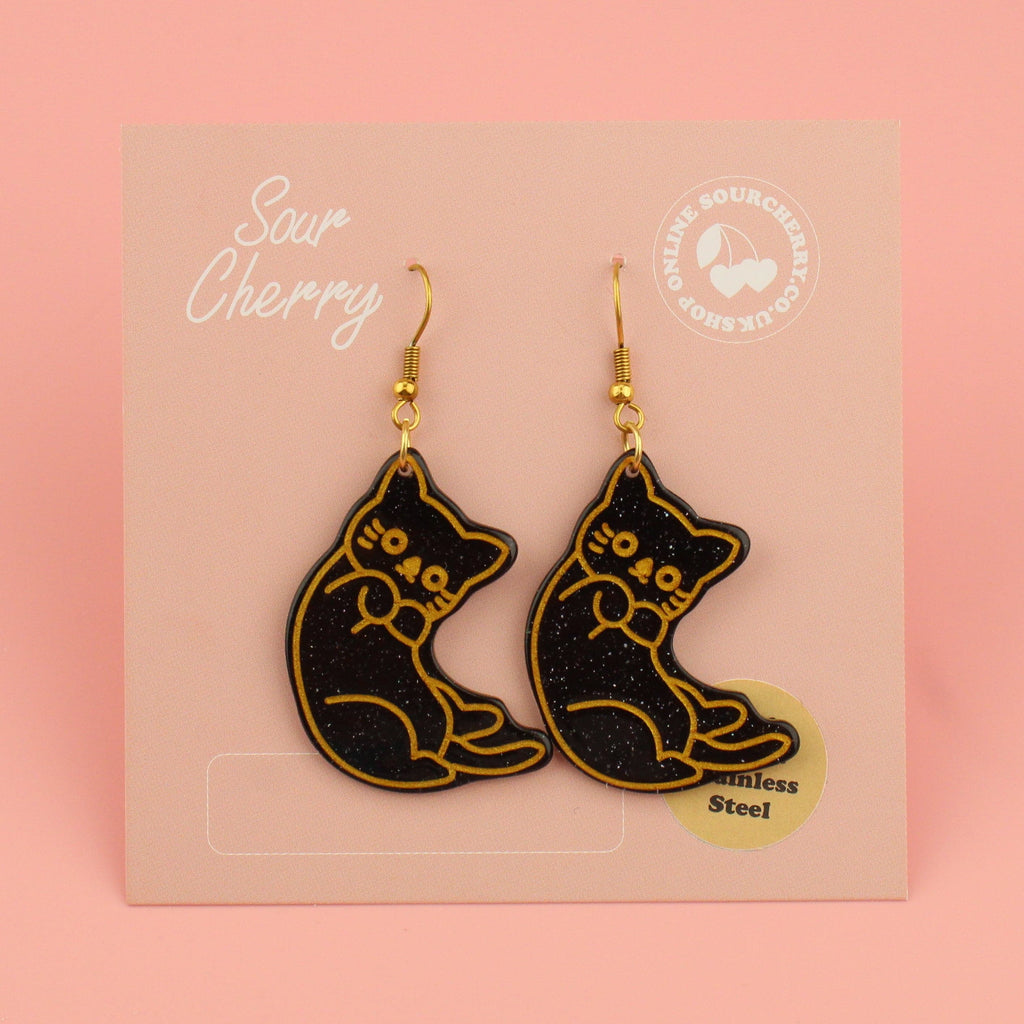 Black glitter cat earrings with gold outlines on gold plated stainless steel earwires shown on cards