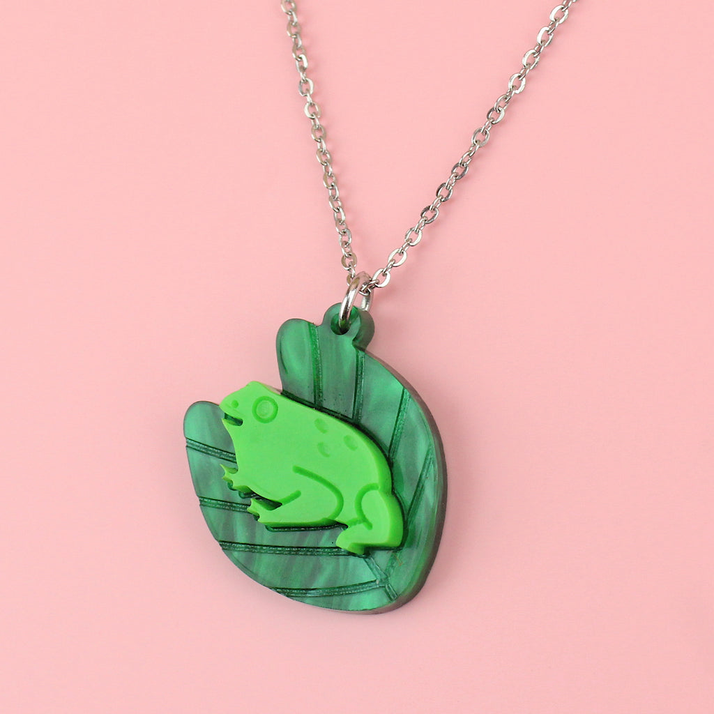 A dark green marble lily pad pendant with a bright green frog in the middle on a stainless steel chain
