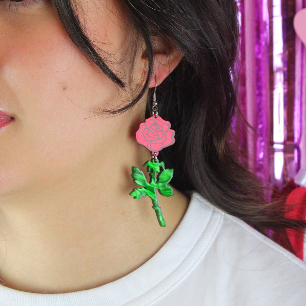 model wearing red mirror acrylic roses and charming green acrylic thorn charms joined together hanging from stainless steel earwires