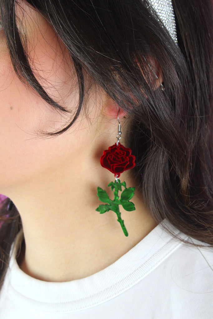model wearing red mirror acrylic roses and charming green acrylic thorn charms joined together hanging from stainless steel earwires