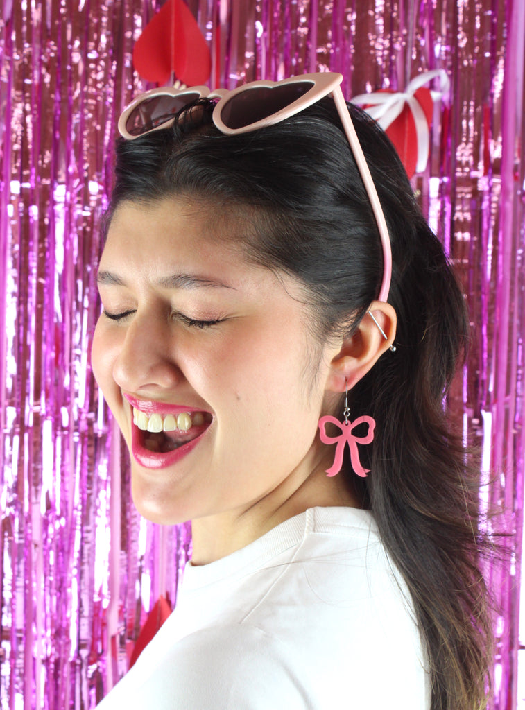 Model wearing rose pink bow shaped charms on stainless steel earwires