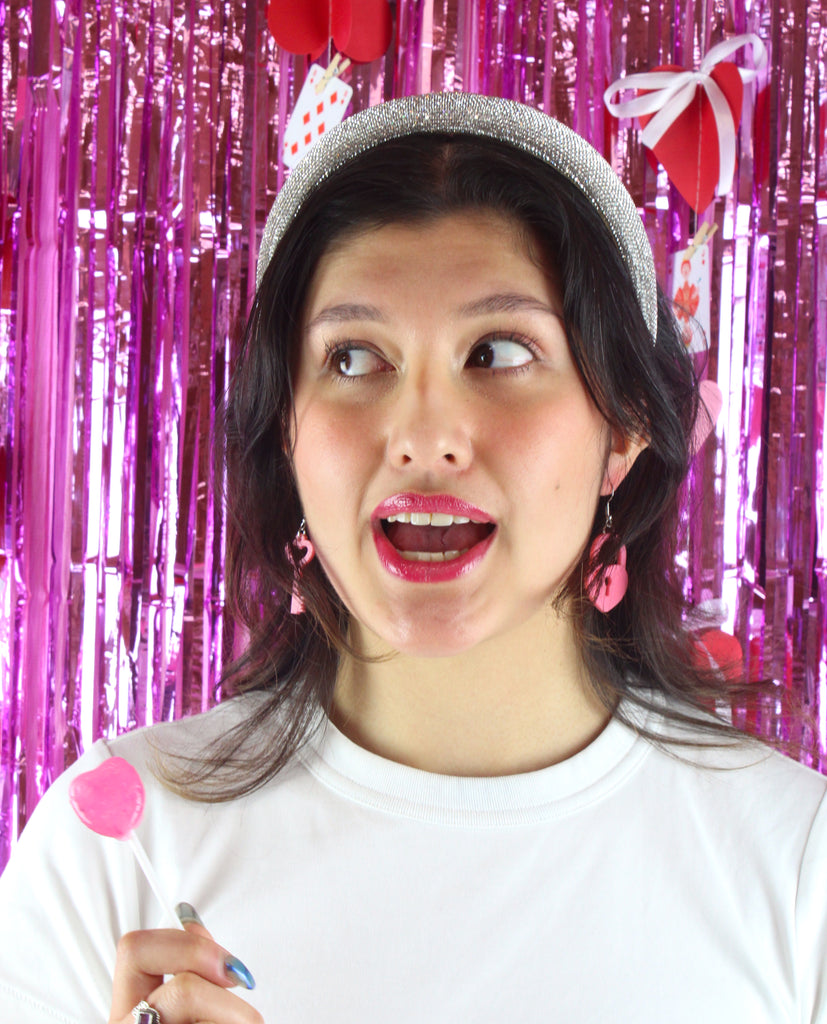 Model wearing Rose pink heart padlock and key charms on stainless steel earwires, holding a pink lollipop