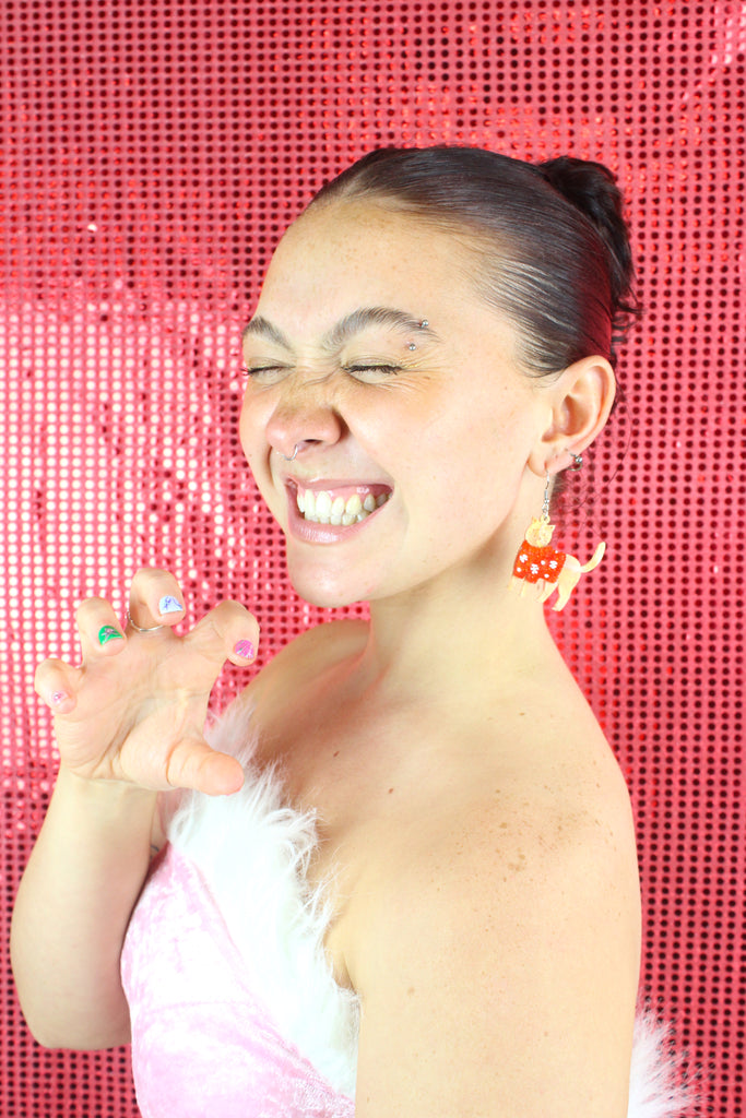 Model wearing earrings that feature acrylic ginger cats with red Christmas jumpers that have snowflakes on them, hanging from stainless steel earwires