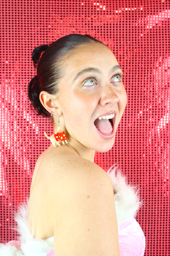 Model wearing earrings that feature acrylic ginger cats with red Christmas jumpers that have snowflakes on them, hanging from stainless steel earwires
