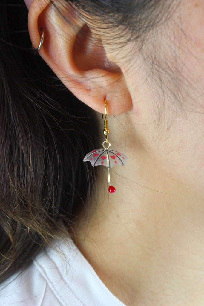 Model wearing 3D umbrella charms with a red heart detail and red handles on gold plated stainless steel earwires