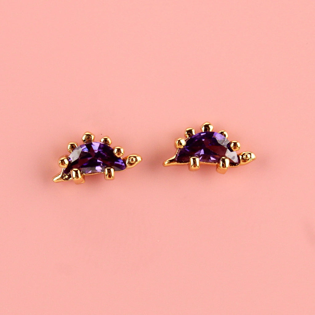 Gold plated brass stegosaurus studs with purple cubic zirconia on the body of the dinosaur