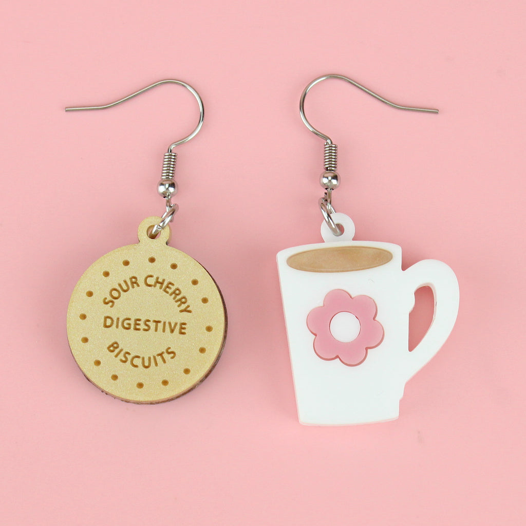 Chocolate digestive charm reading 'Sour Cherry Digestive Biscuits' and a cup of tea charm with a pink flower design, both on stainless steel earwires