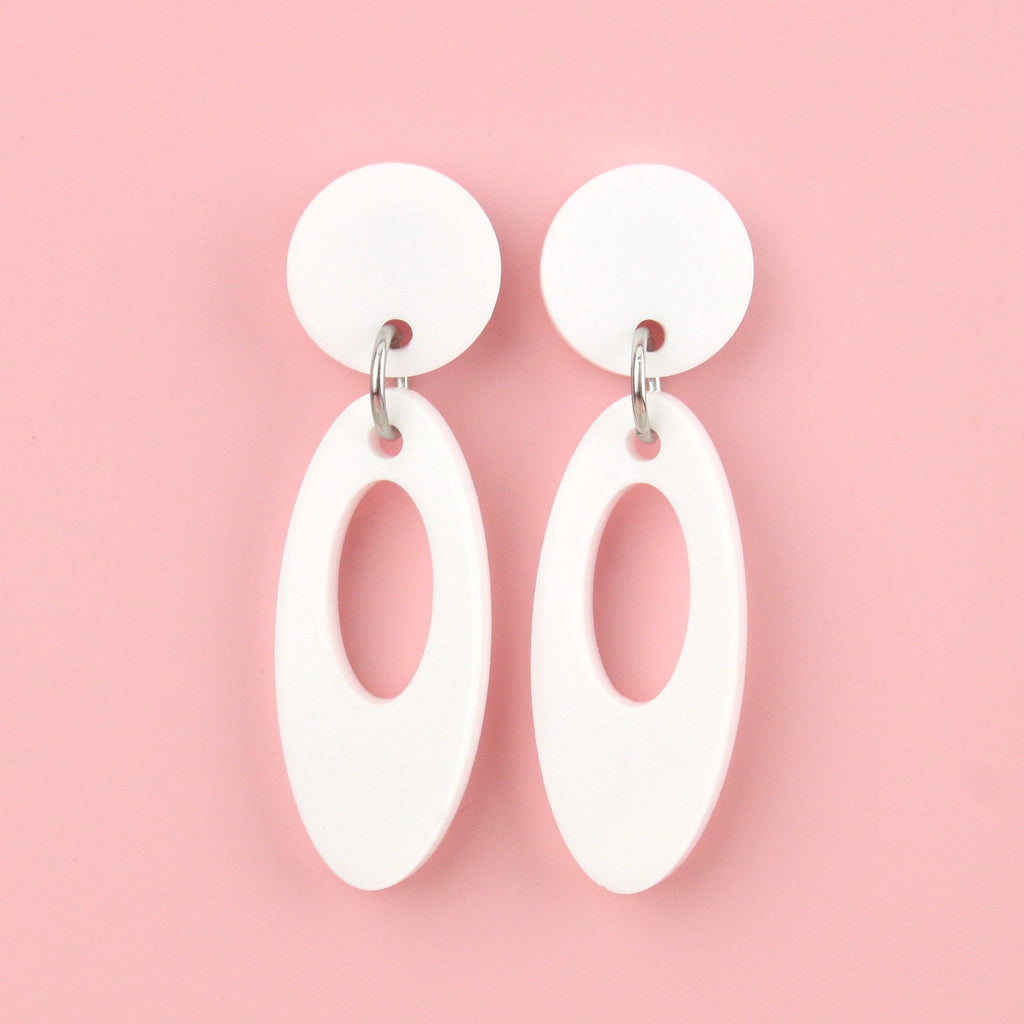 White perspex oval-shaped earrings with a cut out design hanging from a white circle-shaped stud 