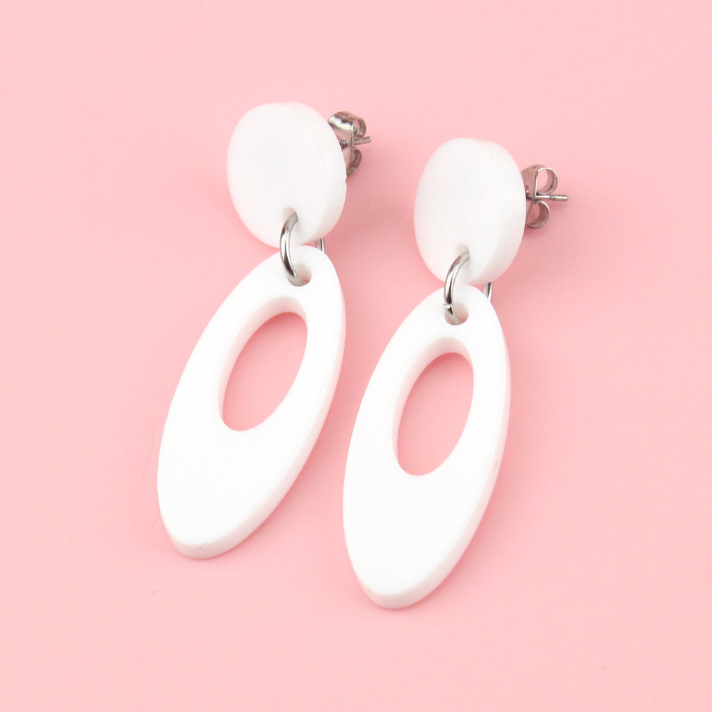White perspex oval-shaped earrings with a cut out design hanging from a white circle-shaped stud 