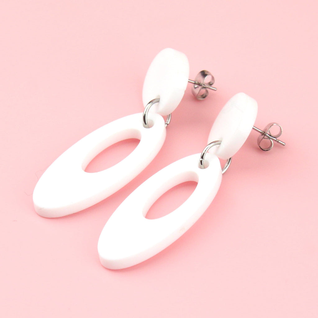 White perspex oval-shaped earrings with a cut out design hanging from a white circle-shaped stud 