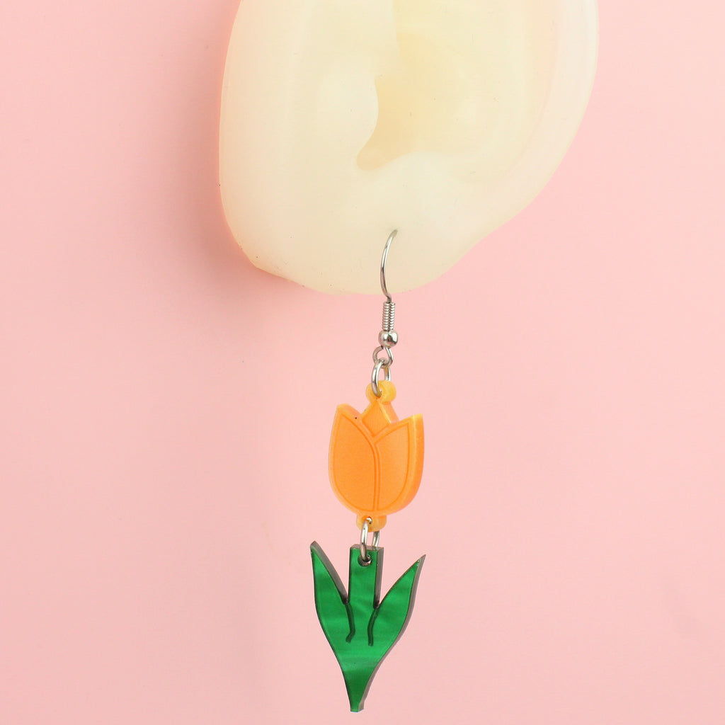 Ear wearing orange tulip charms with green stems on stainless steel earwires