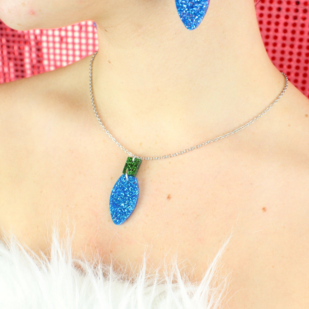 Blue Christmas Light Bulb Pendant with a green top on a stainless steel chain, model is also wearing matching earrings