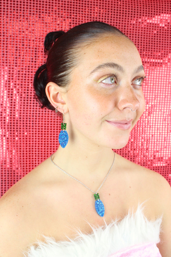 Blue Christmas Light Bulb Pendant with a green top on a stainless steel chain, model is also wearing matching earrings