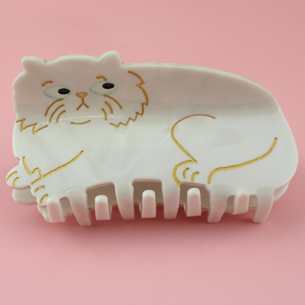 White persian cat claw clip with gold outlines of the face and the legs. The cat is making a side eye.