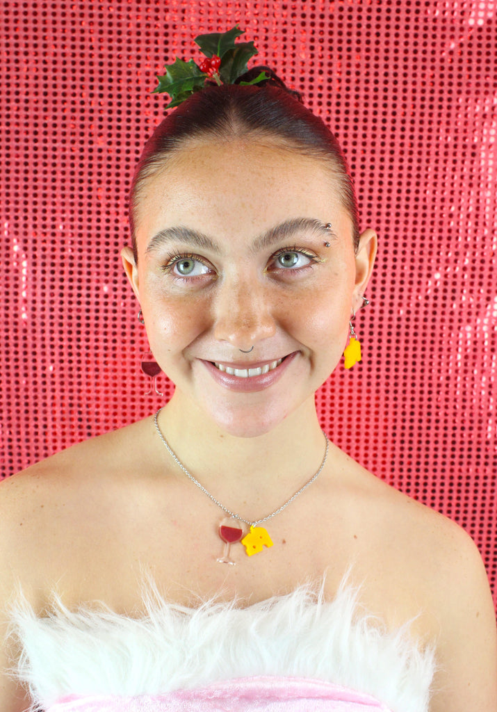 Model wearing one swiss cheese earring and another earring featuring a glass of red wine with the matching necklace