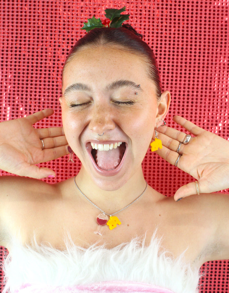 Model wearing one swiss cheese earring and another earring featuring a glass of red wine with the matching necklace