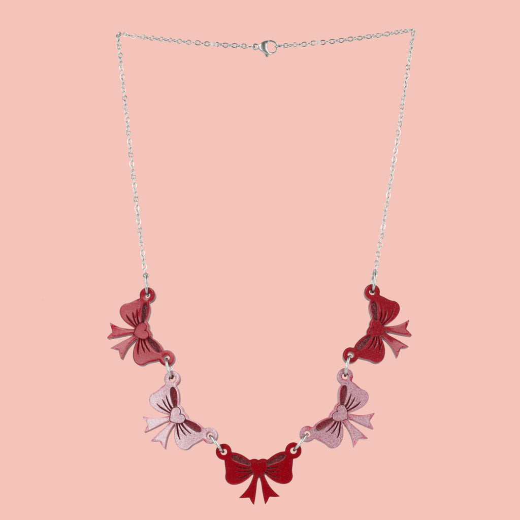 Necklace with red and pink bow-shaped pendants on a pink background