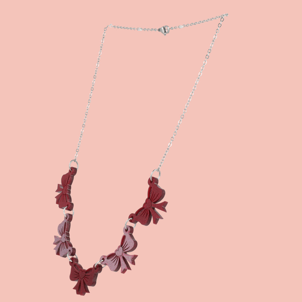 Necklace with red and pink bow-shaped pendants on a pink background