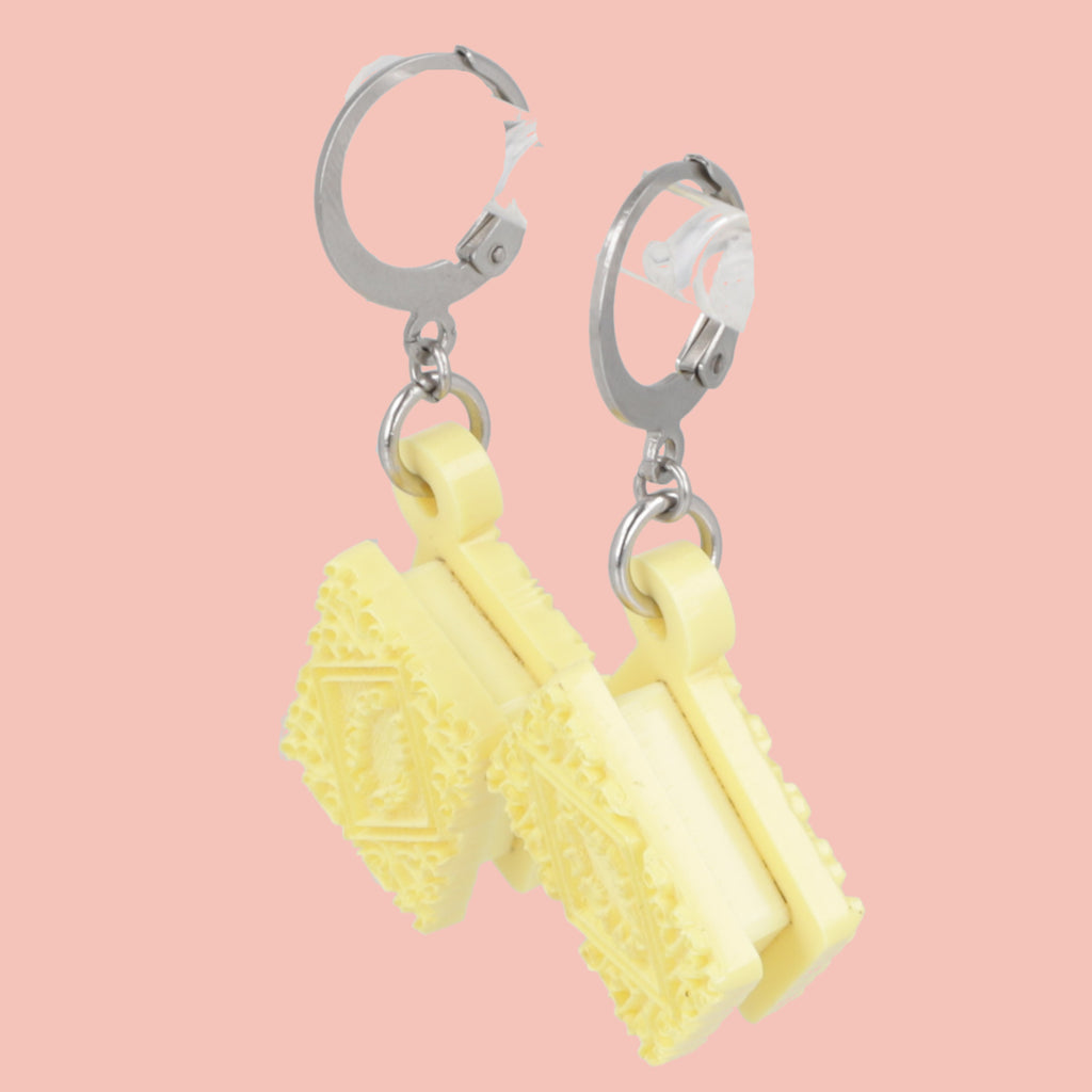 Yellow earrings shaped like custard creams on a pink background
