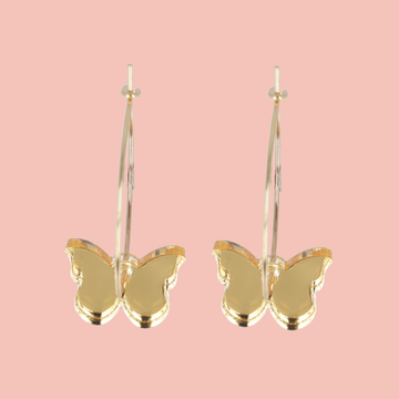 Gold butterfly earrings on a pink background