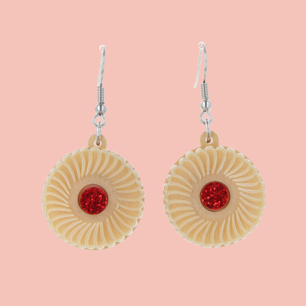 Pair of earrings with jam and cream biscuit charms on a pink background