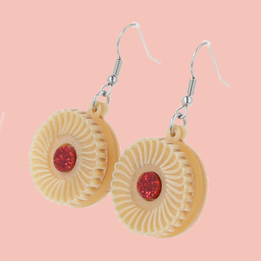 Pair of earrings with jam and cream biscuit charms on a pink background