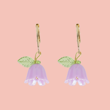 Pair of purple flower-shaped earrings with green leaves on a pink background