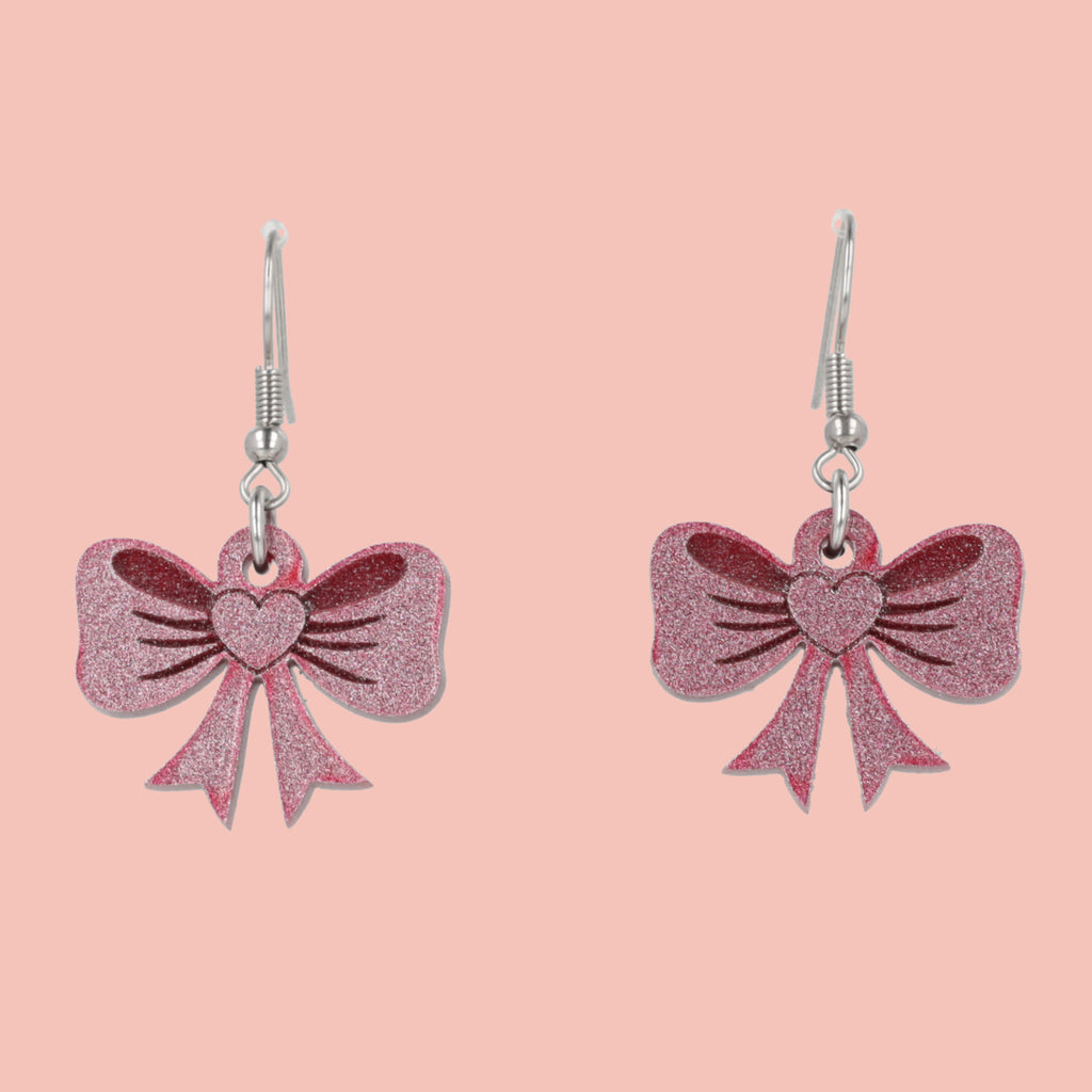 Pink glittery bow earrings on a pink background