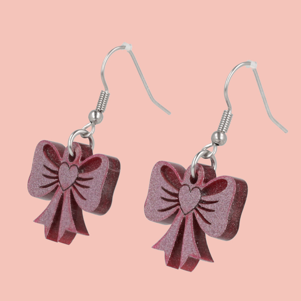 Pink glittery bow earrings on a pink background