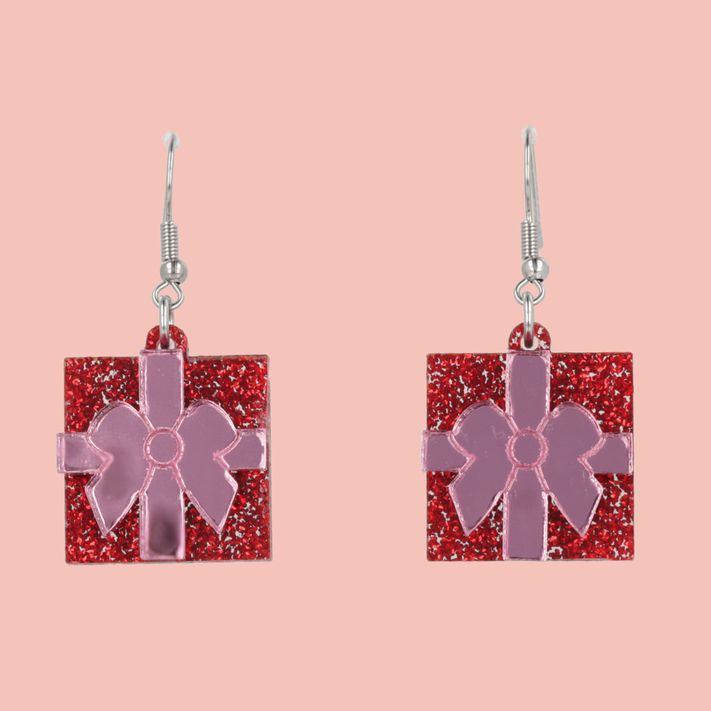 Earrings with red glittery gift box and pink bow design on a pink background