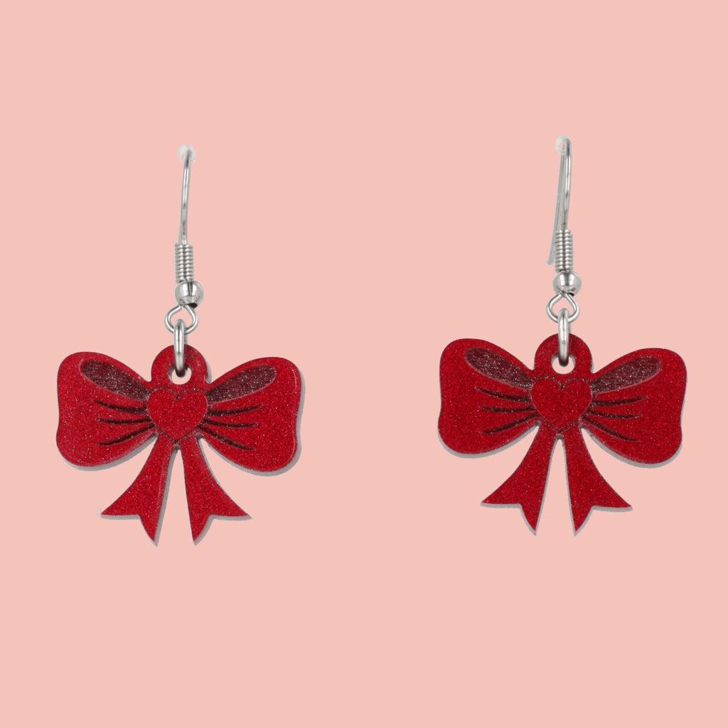Red bow-shaped earrings on a pink background