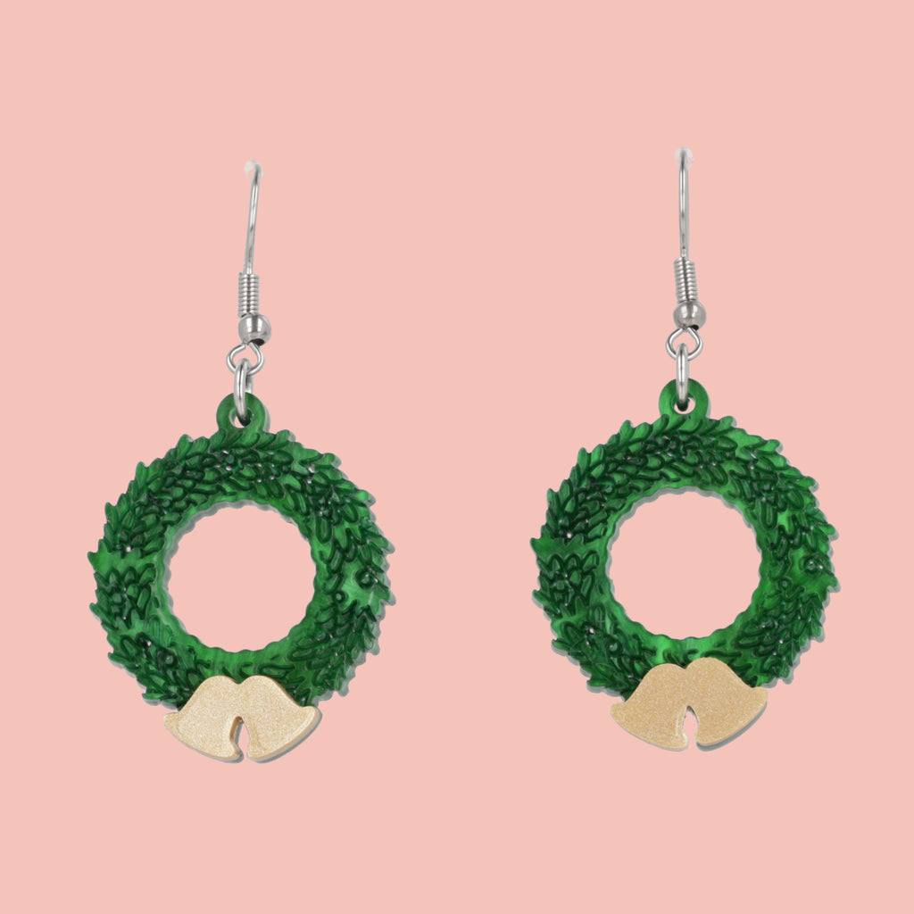 Green wreath earrings with gold accents on a pink background