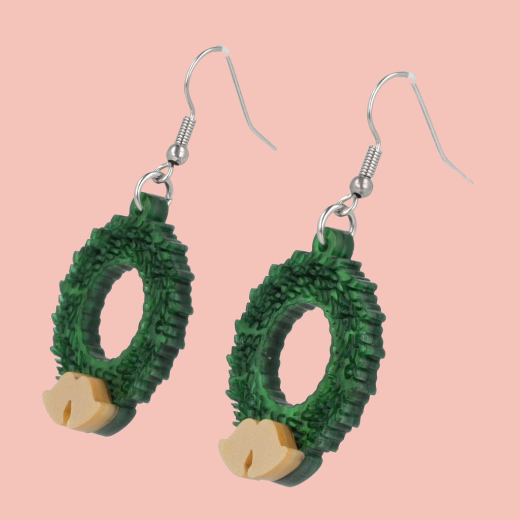 Green wreath earrings with gold accents on a pink background