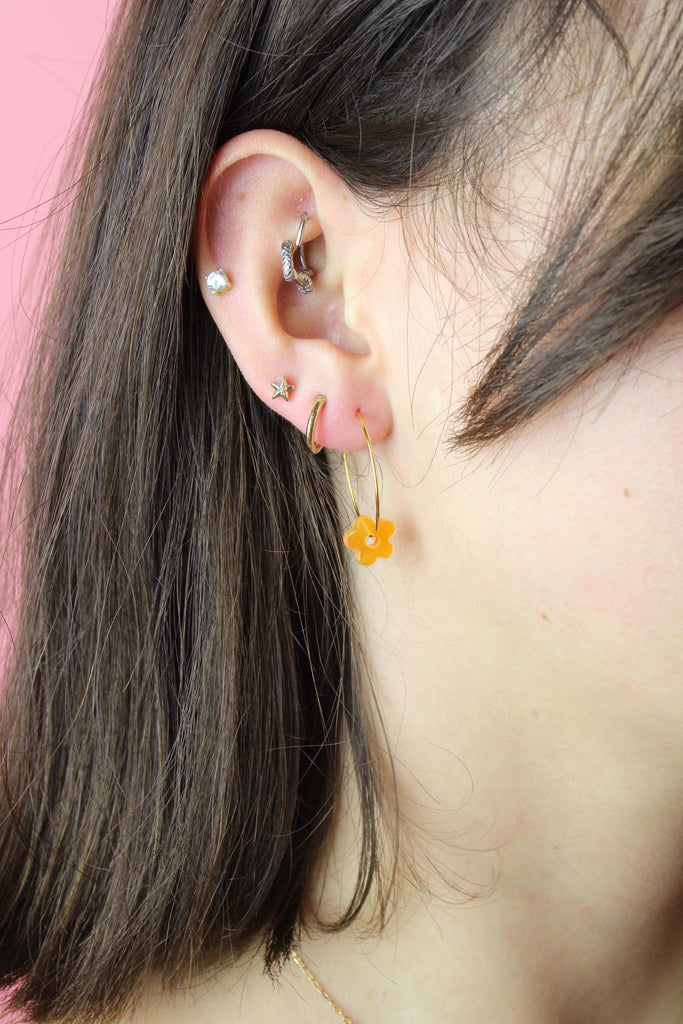 Model wearing the orange flower charms on the gold hoops