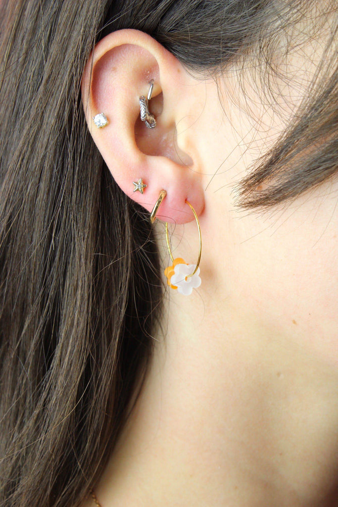 Model wearing both the orange and white flower charms on a gold hoop