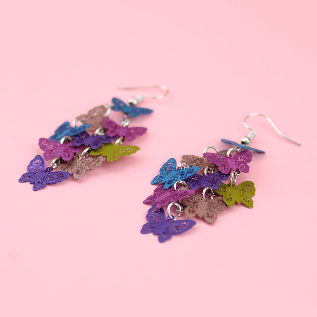 A cluster of blue, rose gold, pink, purple and gold butterfly charms on stainless steel earwires