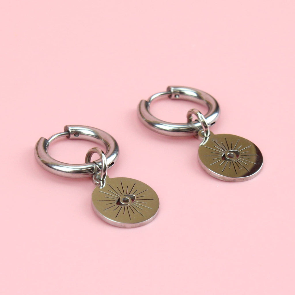atainless steel hoops with a circular charm featuring a cut out evil eye