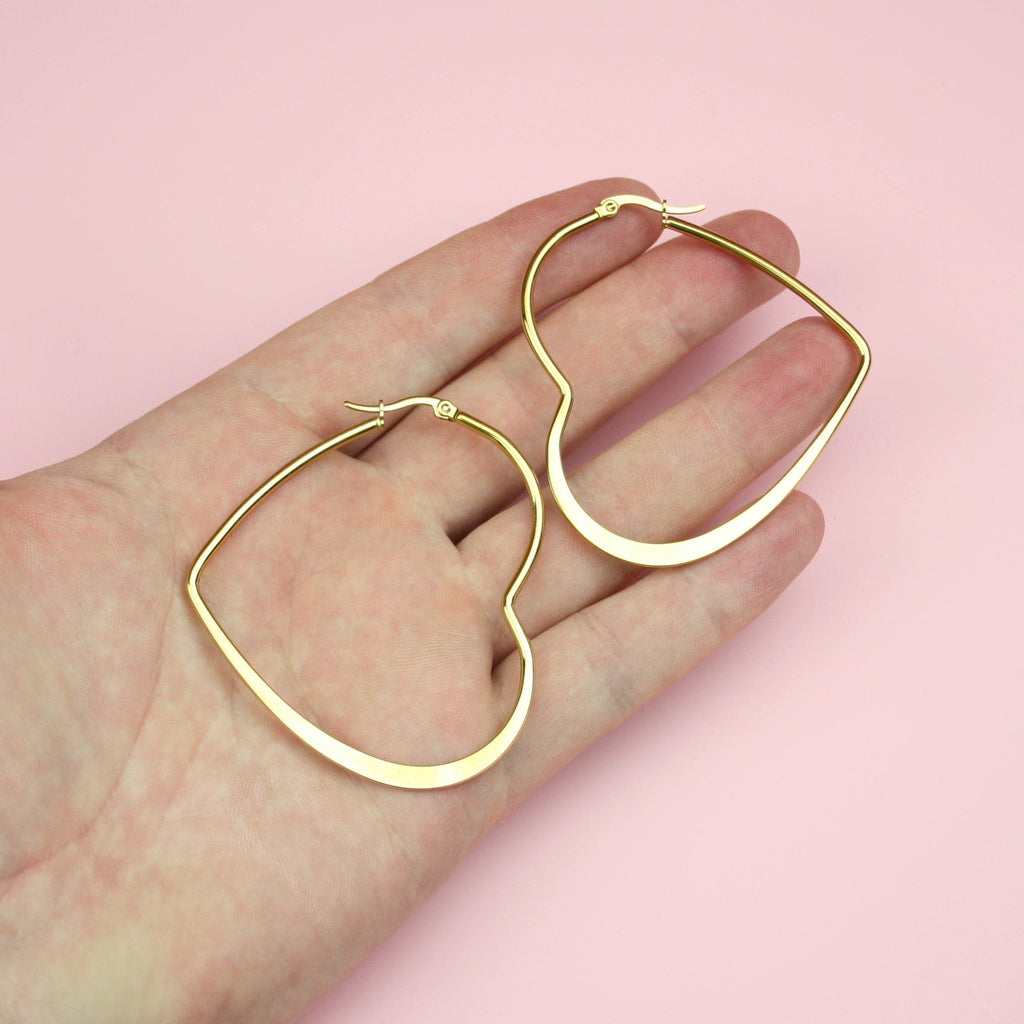Hand holding gold plated stainless steel heart shaped hoops for scale