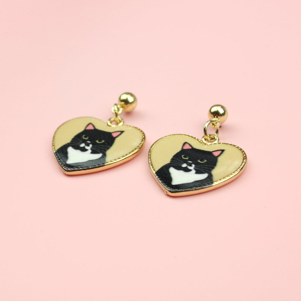 Gold heart shaped charms with a black cat portrait inside them on gold plated stainless steel studs