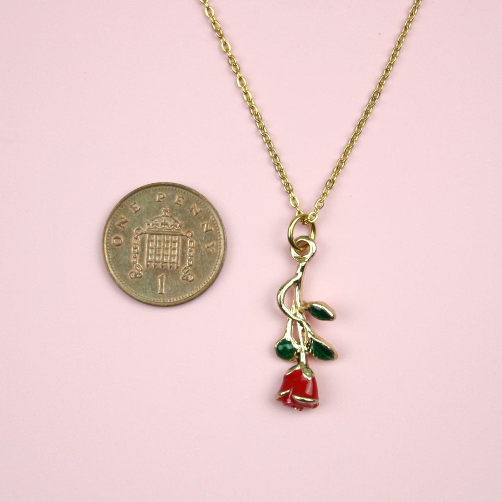 Red Enchanted Rose charm with a green stem on a gold plated stainless steel chain, showing a penny next to the charm for scale