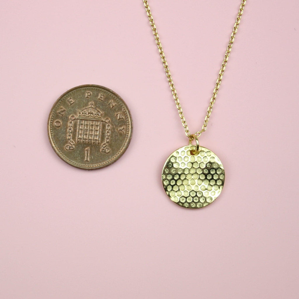 Gold plated stainless steel necklace featuring a gold disk honeycomb pendant with a penny next to it for scale