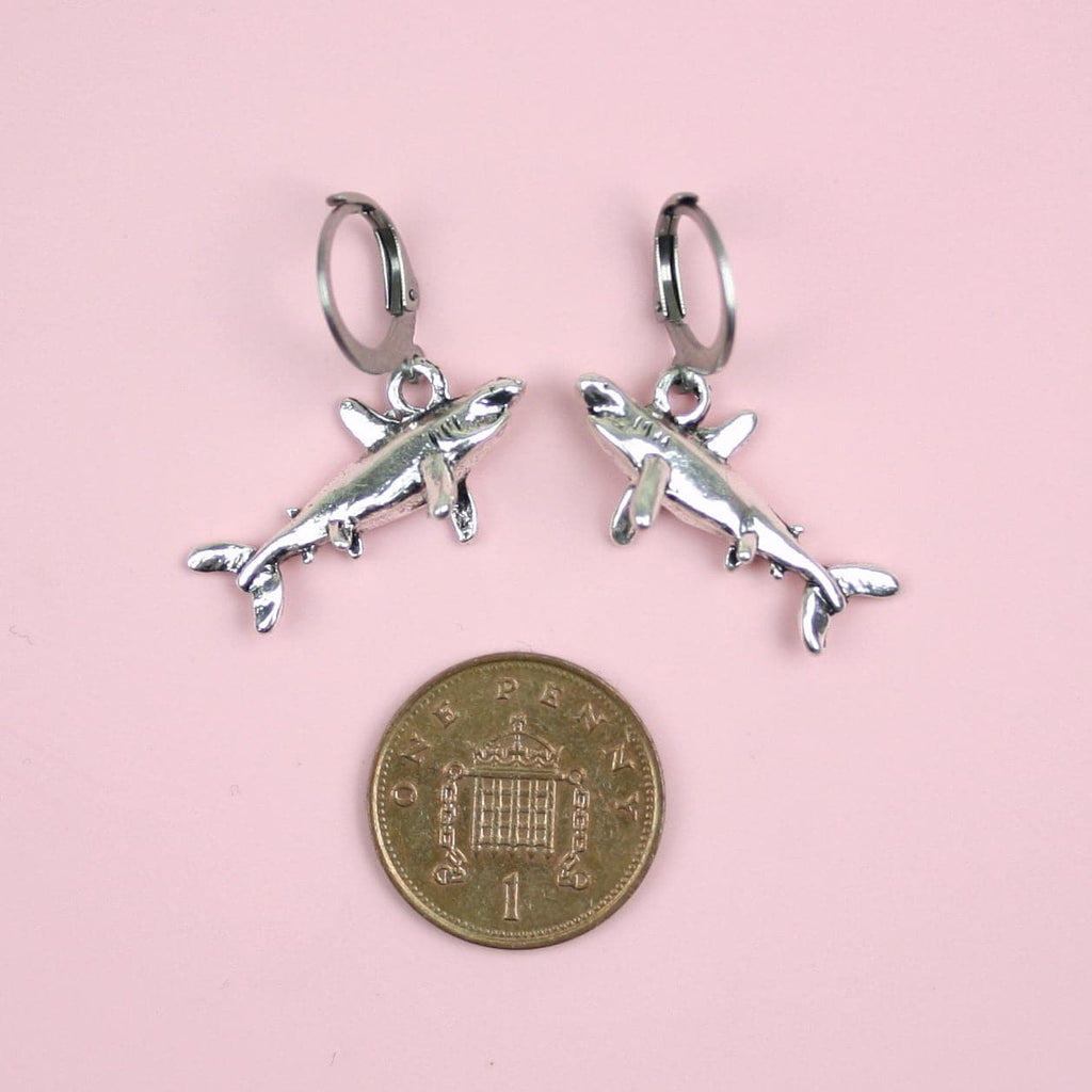 3D Shark charms on stainless steel huggie hoops with a penny underneath it for scale