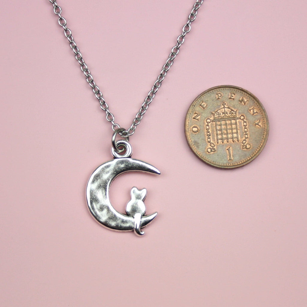 Stainless steel chain featuring a crescent moon pendant with a silhouette of a cat perced at the bottom of the moon, showing a penny next to it for scale