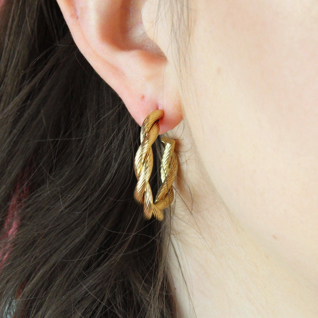 Ear wearing gold hoop earrings with a knotted effect