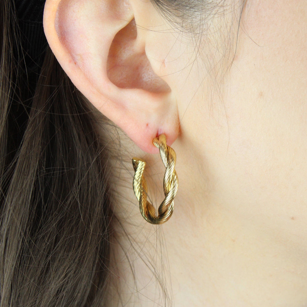 Ear wearing gold hoop earrings with a knotted effect