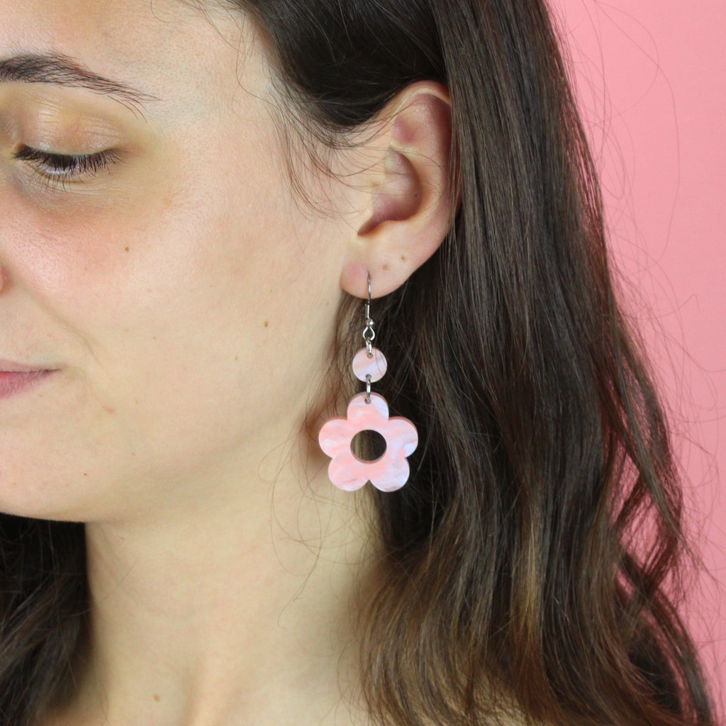 Model wearing pastel peach and blue perspex flower charms with cut out middle on stainless steel earwires
