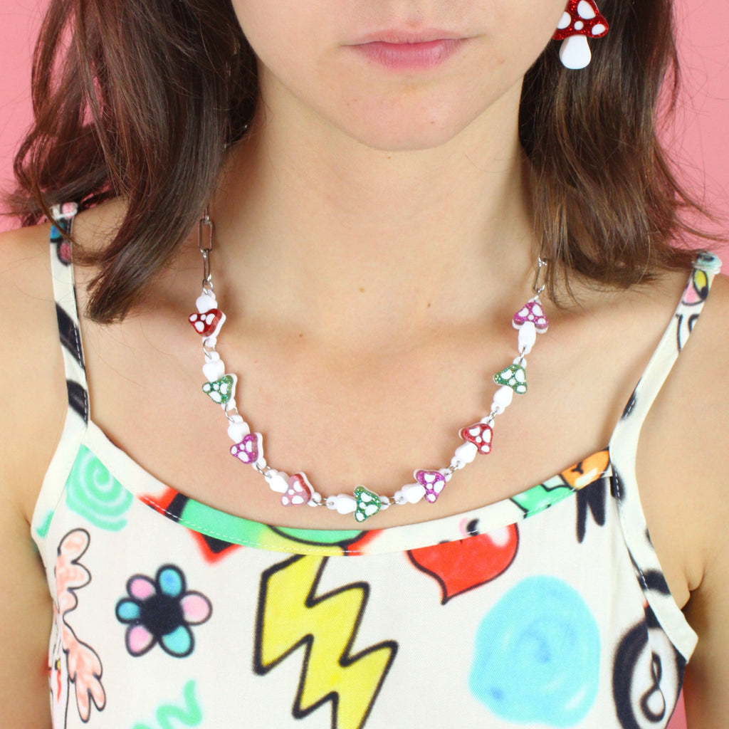 Model wearing oval chain necklace with red, green and pink glittery mushroom charms 
